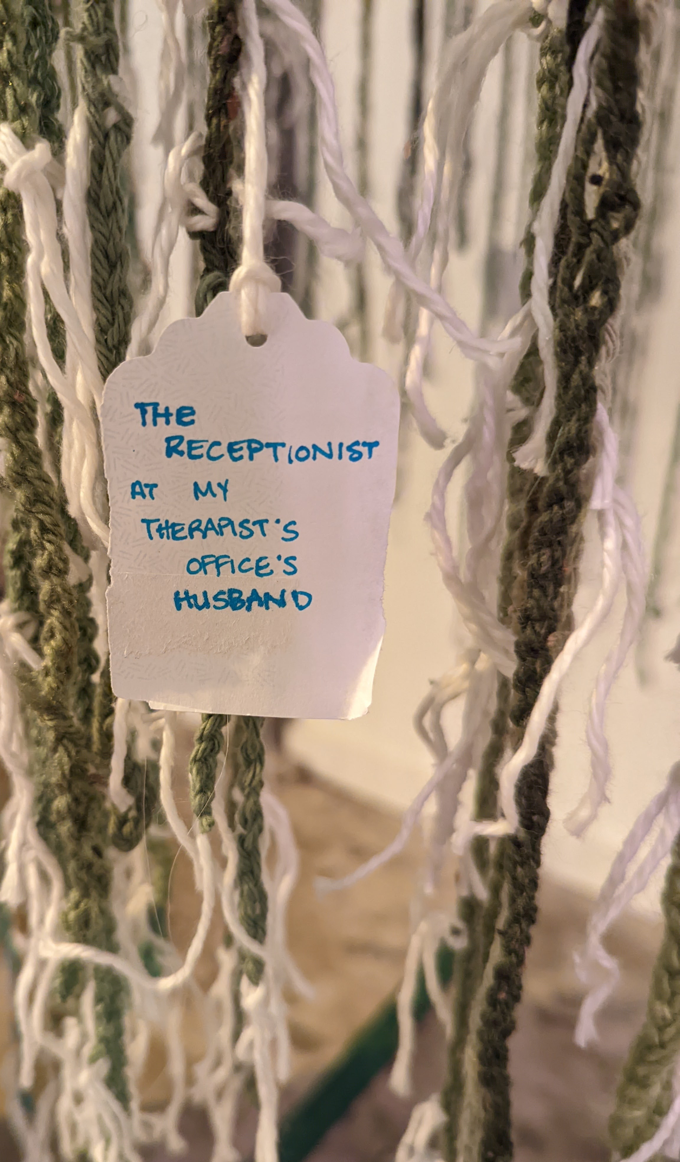 A handwritten tag hangs from green crocheted strands. It reads "The receptionist at my therapist's office's husband."
